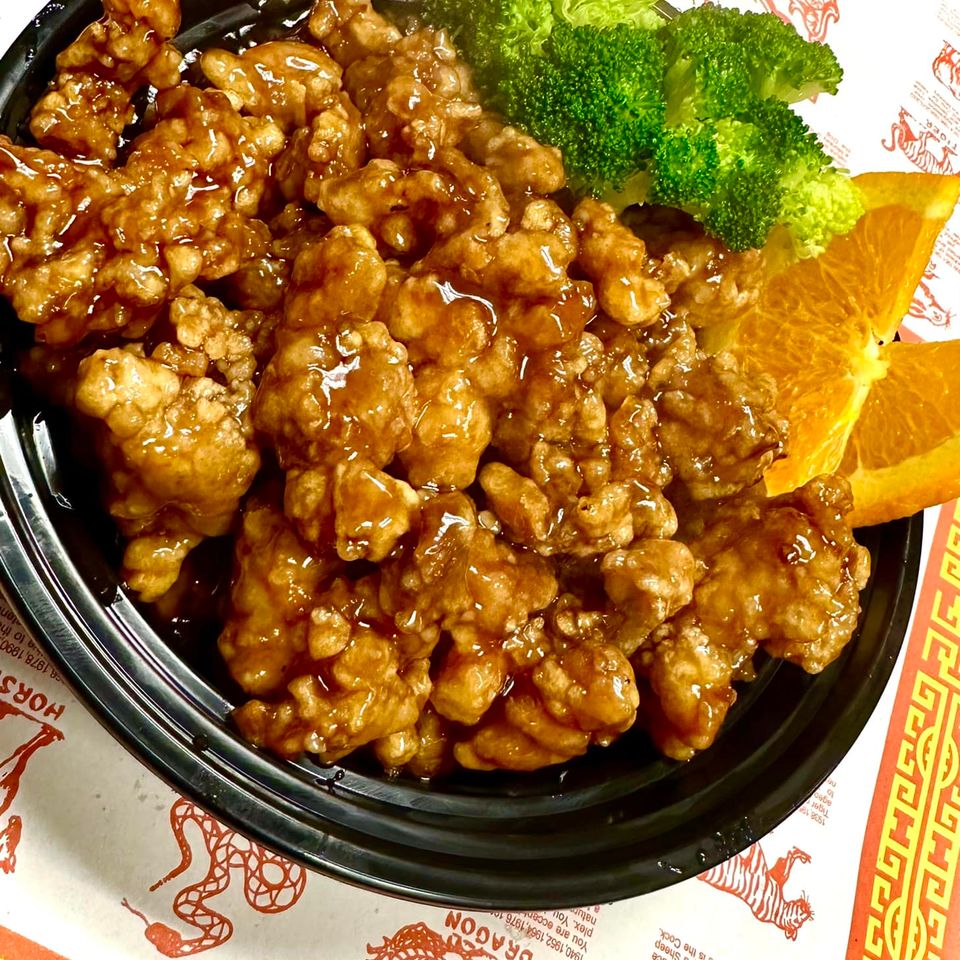 Crispy Orange Chicken coated in glossy orange sauce with broccoli florets and fresh orange slices at Little Hunan.