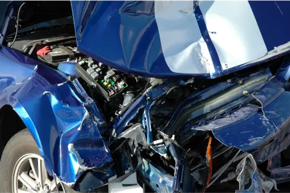 Close-up of severe front-end collision damage on a blue vehicle, illustrating the need for professional frame repair and bodywork.