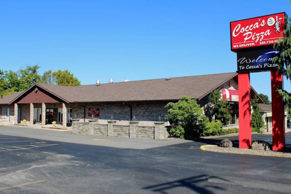 Front entrance of Cocca’s Pizza Boardman Ohio location with brick exterior, large windows, and planters by the doorway.