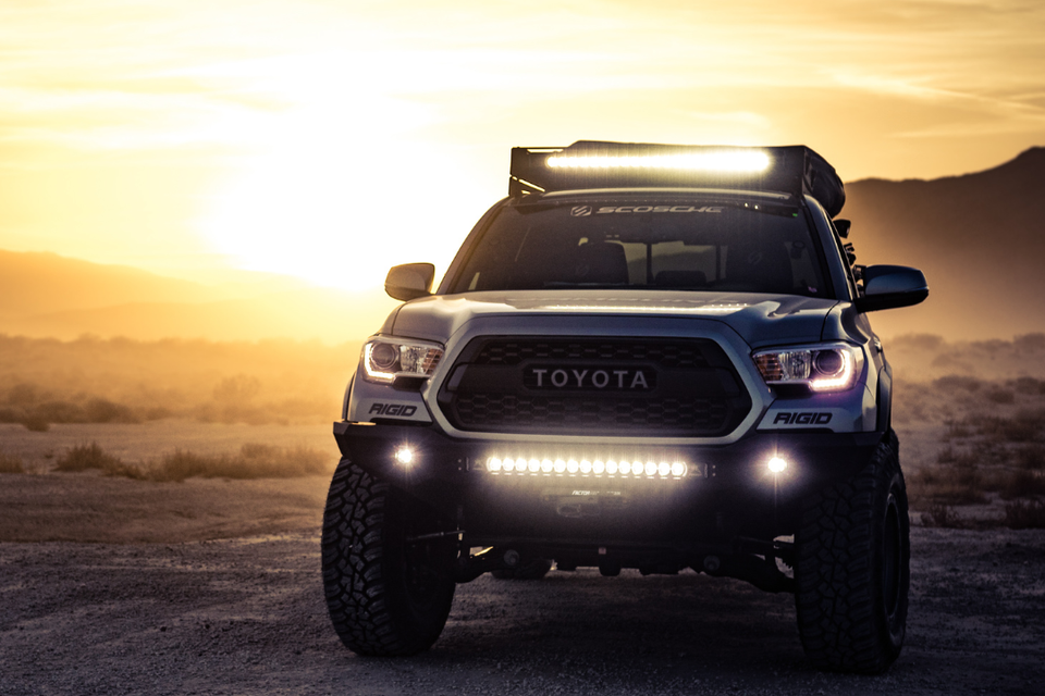 Front view of a lifted off-road truck with LED light bars parked outdoors at sunset.
