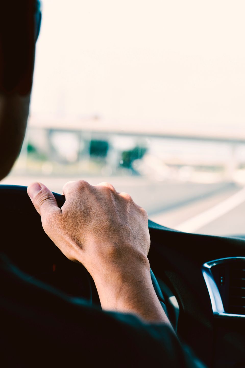 Closeup of a man, seen from behind, driving a car in a road with several lanes