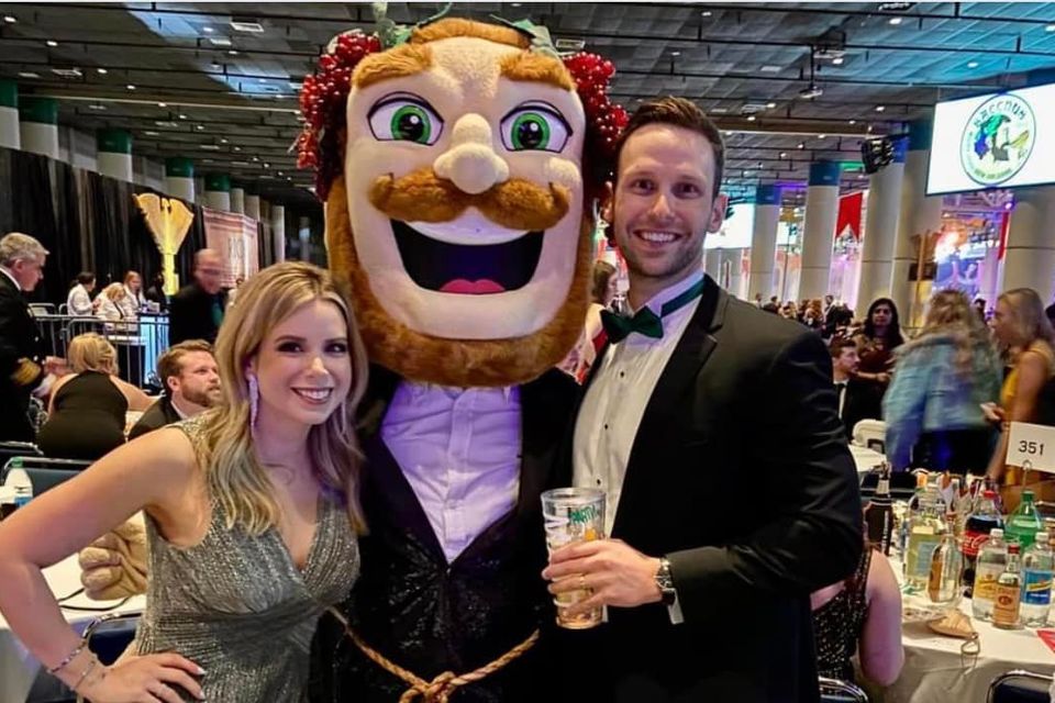 Couple posing with a costumed mascot at a Mardi Gras ball, with the man wearing a black tuxedo.”