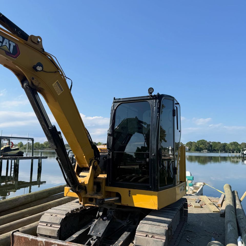 Cat excavator with tinted cab windows working on a waterfront dock in Moyock NC