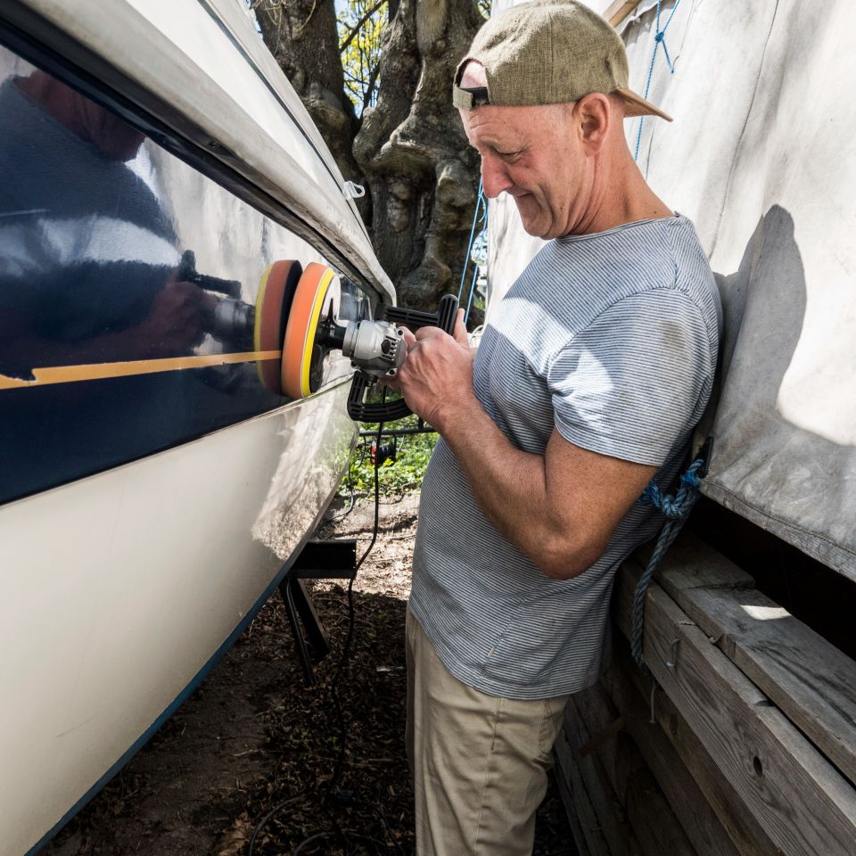 A man uses a power tool to wax the side of a motorboat