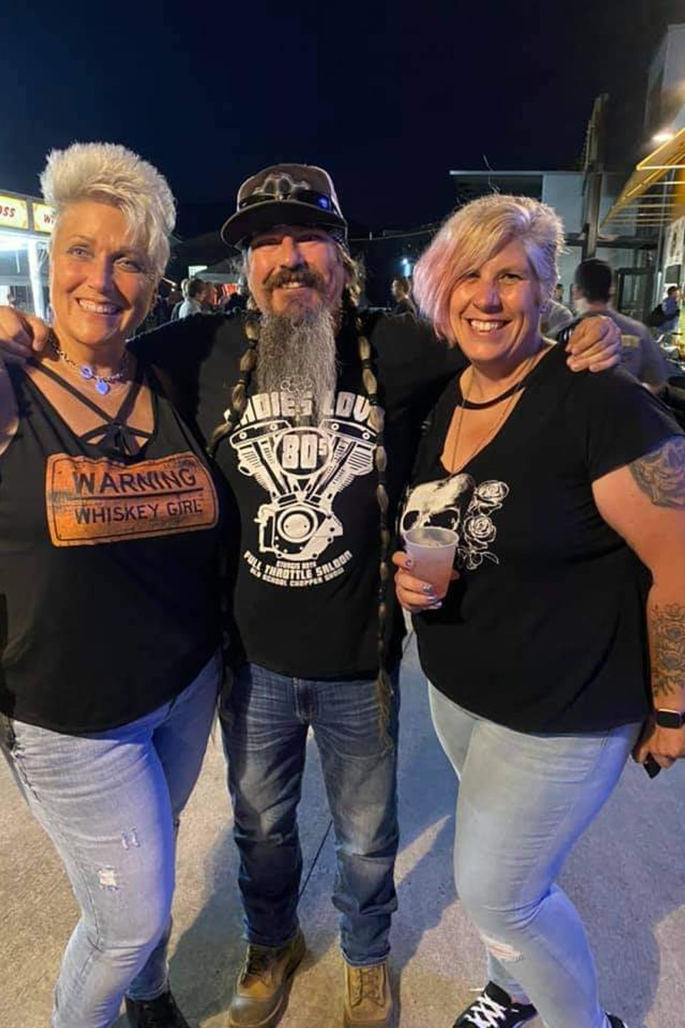 Three attendees posing together outdoors during an evening biker event.