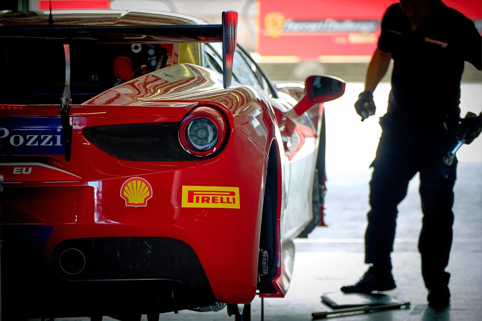Image of Race Car with Pirelli Sponsor and the mechanic close by has taken off the driver side wheels, photo is of drivers side of car 1/2 view from rear