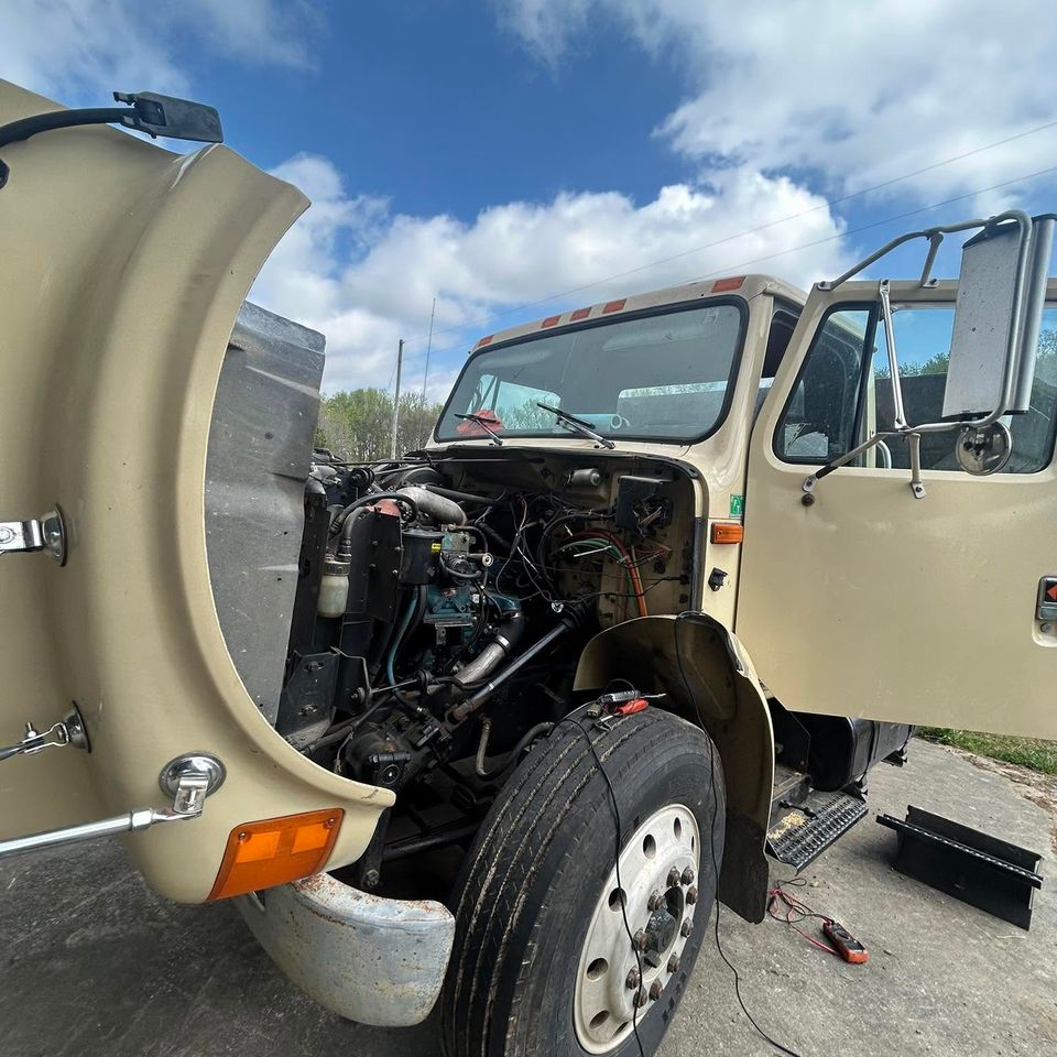 Tan International medium-duty truck with hood tilted open for diesel engine repair in Arab Alabama