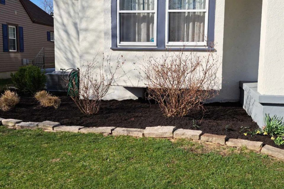 Front landscape bed with fresh black mulch, shrubs, and decorative stone edging along the home.