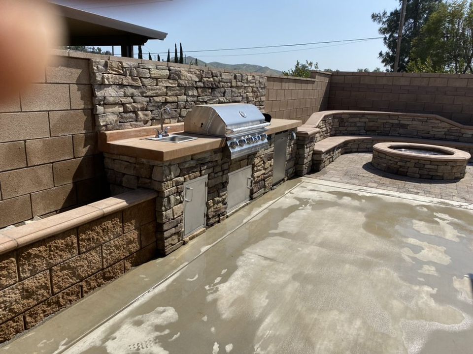 Custom outdoor kitchen with built-in BBQ, fire pit, and decorative stone seating wall