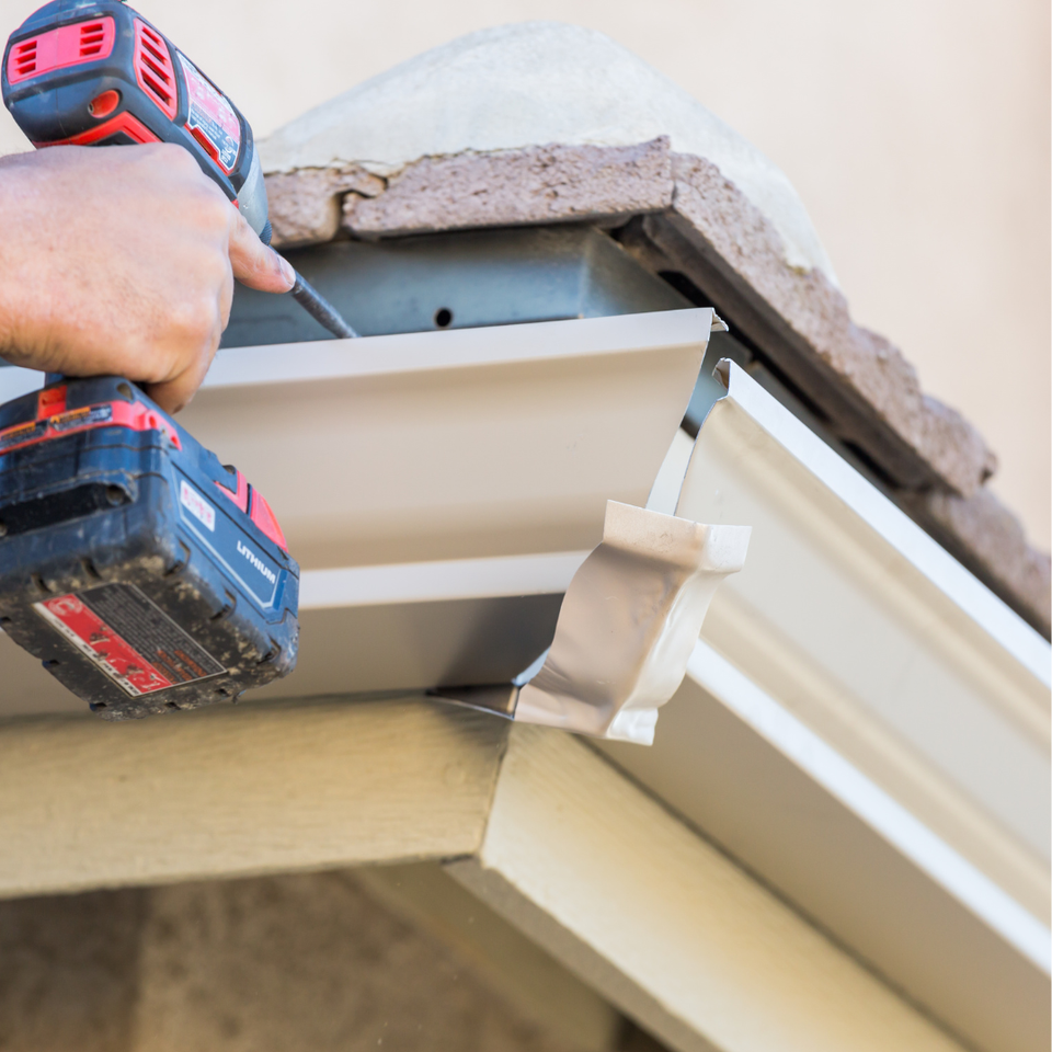 Technician installing a residential gutter system along the edge of a home's roof.