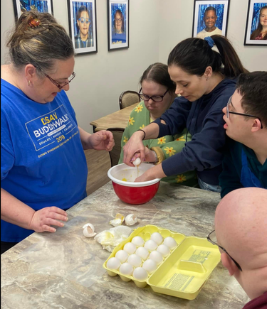 Participants with Down syndrome receiving guidance from instructors while preparing ingredients for a recipe.