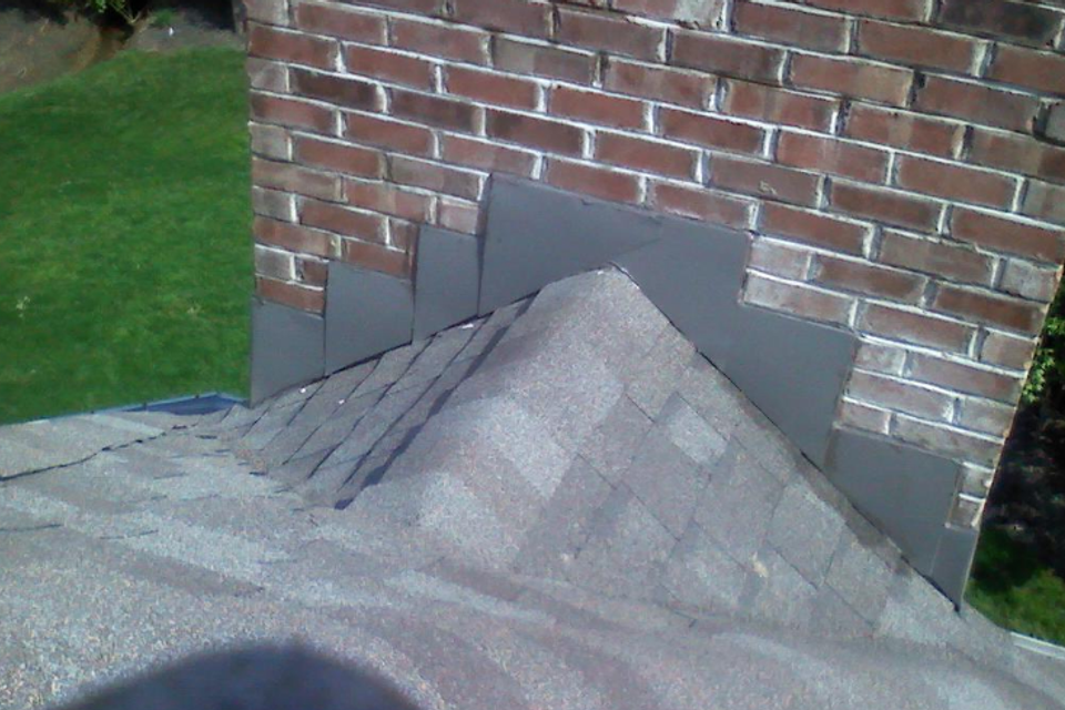 Close-up of chimney flashing and architectural asphalt shingles professionally installed to provide a watertight roof seal by E & D Roofing, Inc.