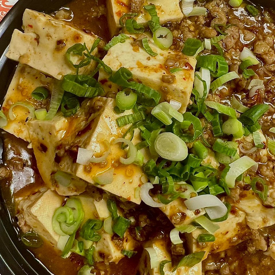 Savory Asian-inspired entrée topped with green onions and served in a black bowl at Little Hunan.