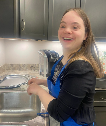 Participant with Down syndrome smiling while washing dishes during a DSAV Cooks life skills class.