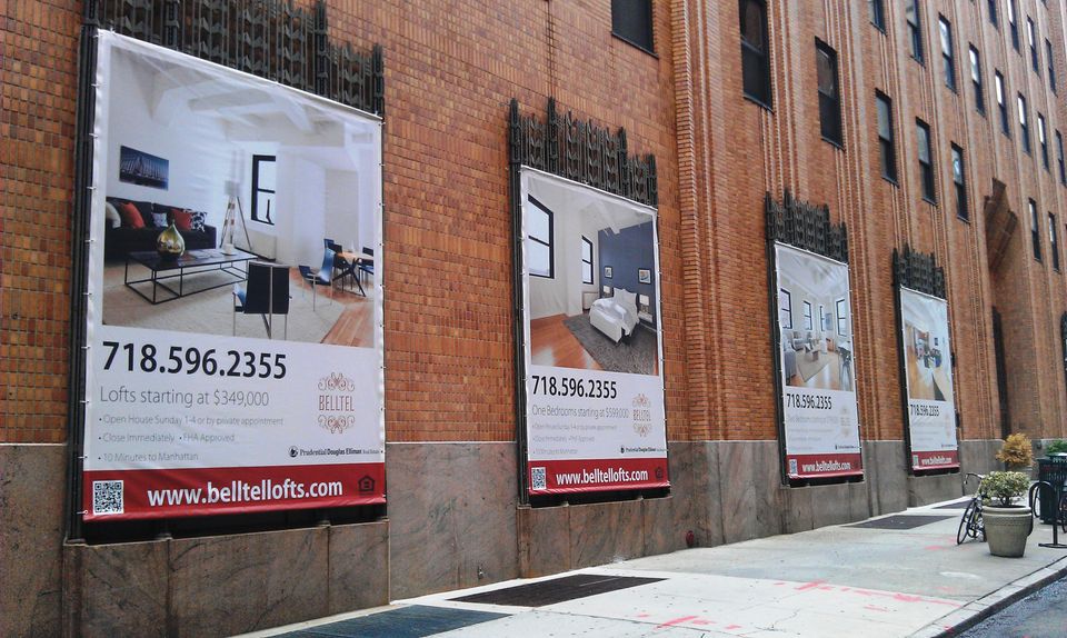 Row of printed vinyl banners advertising Belltel Lofts on a brick building facade in Brooklyn