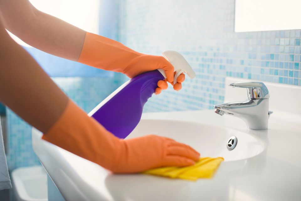 Gloved cleaner spraying and wiping bathroom sink during house cleaning service in Virginia Beach VA