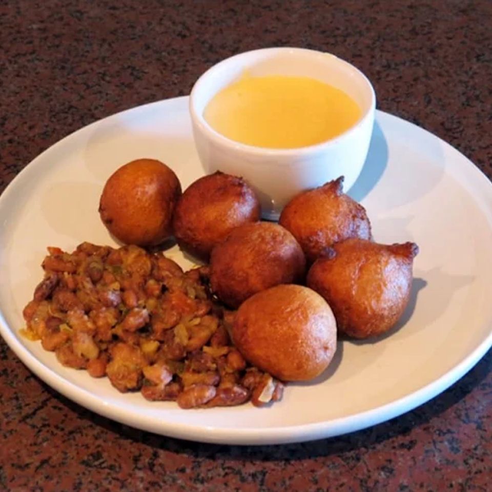 Golden fried puff puff dough balls with seasoned beans and a cup of dipping sauce