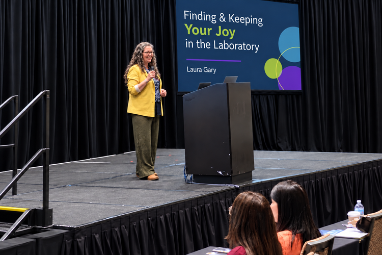 Laura Gary speaking beside her Finding & Keeping Your Joy in the Laboratory presentation screen.