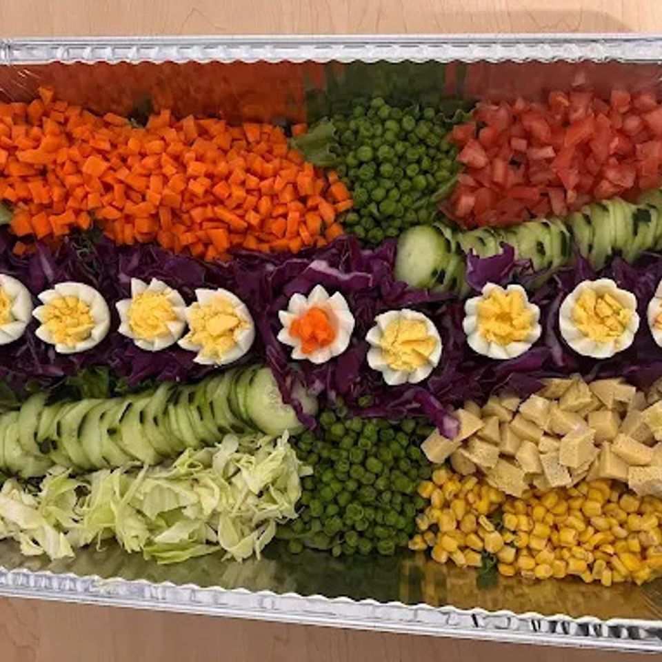 Layered catering salad tray with boiled eggs, purple cabbage, carrots, peas, corn and cucumber