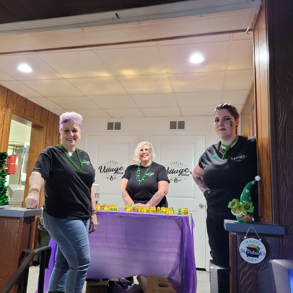 Kelly, Tracy, and another volunteer standing behind a decorated registration table with St. Patrick’s Day-themed decorations and raffle items.