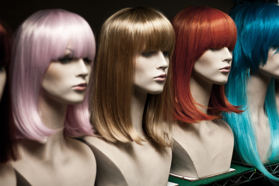 Mannequin heads displaying wigs in pastel pink, blonde, red, and bright blue with sleek, shoulder-length styles and full bangs.