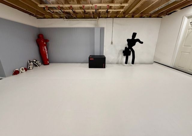 Wide view of white training mats, grappling dummy, and striking pads in an Okemos private martial arts studio