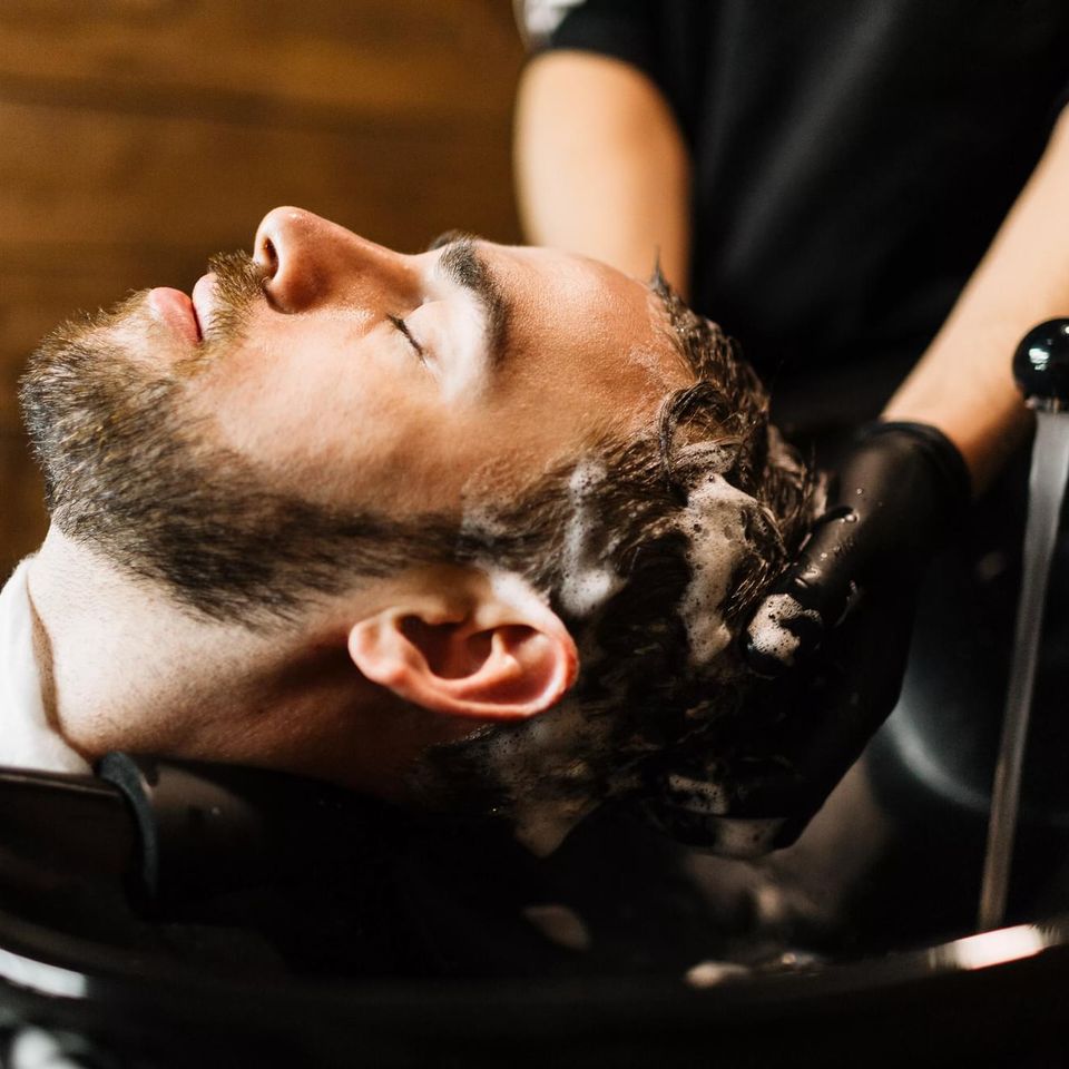 Close-up of a person reclining with their head in a sink, receiving a professional hair wash from a stylist wearing black gloves.