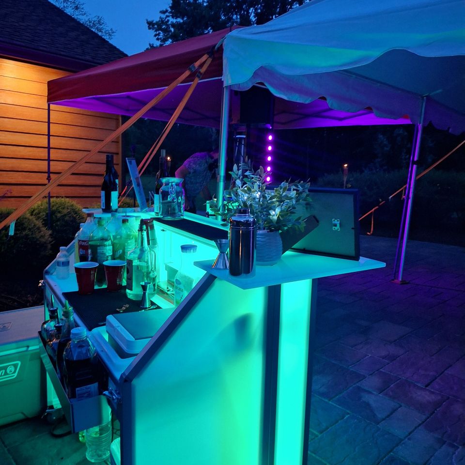 Poppin Cocktails mobile bar setup at night with illuminated bar, drink station, and outdoor event lighting