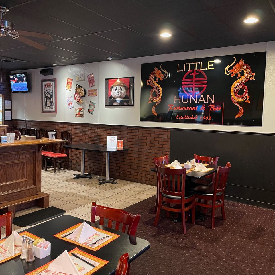 Interior dining room of Little Hunan Restaurant & Bar with tables, seating, and restaurant signage.