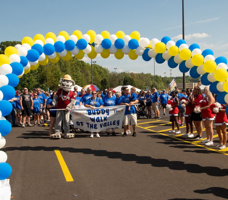 Participants gather beneath a blue, yellow, and white balloon arch at the Down Syndrome Association of the Valley Buddy Walk, marking the start of the community event.