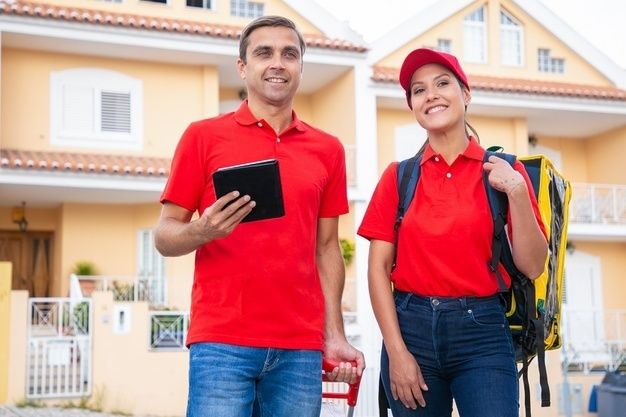 Trabajadores correos alegres pie sonriendo trabajando juntos mensajeros felices entregando pedido bolsa termica vistiendo camisetas rojas hombre que sostiene tableta servicio entrega concepto compra online 7485 (1)