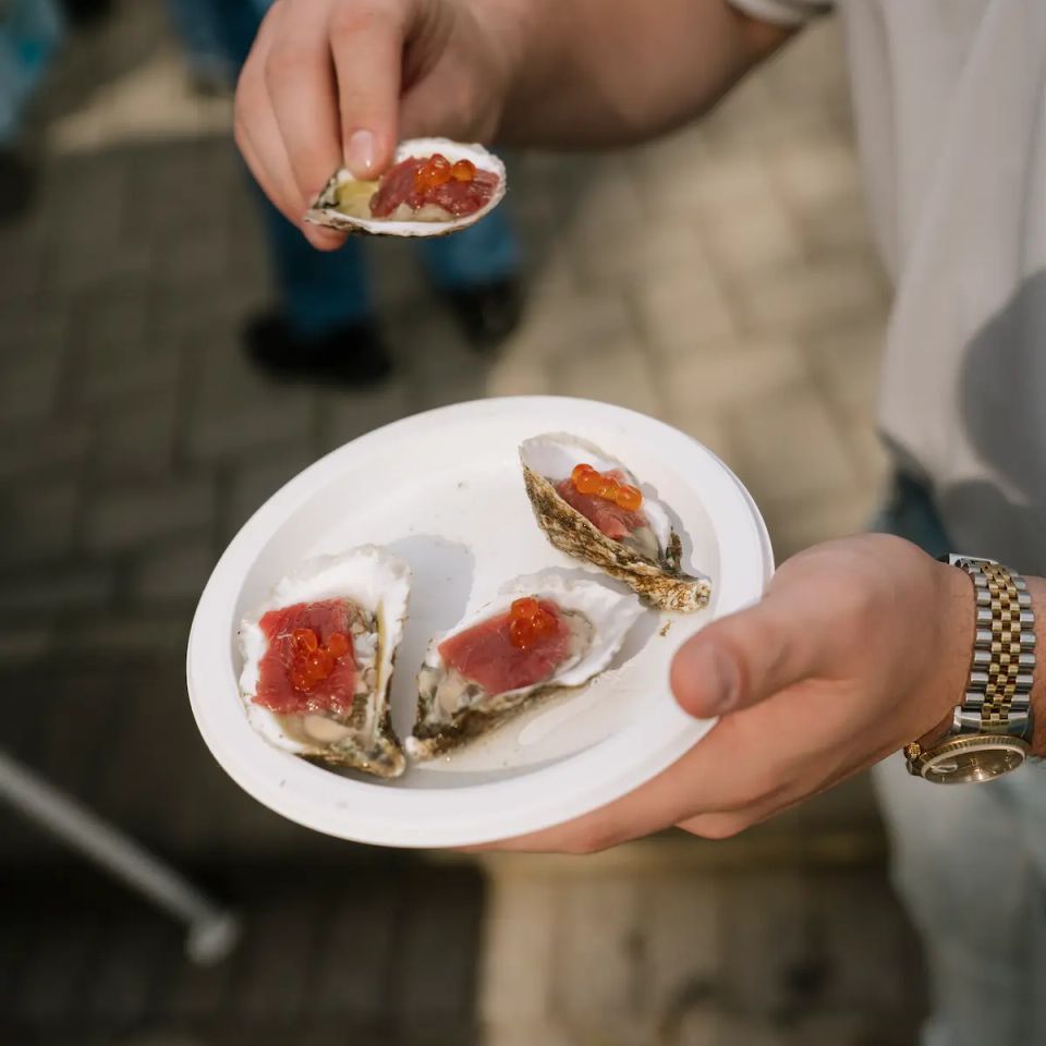 A man holding a clam and other food from a raw bar, provided by Shore2Shore Shucking of Long Island