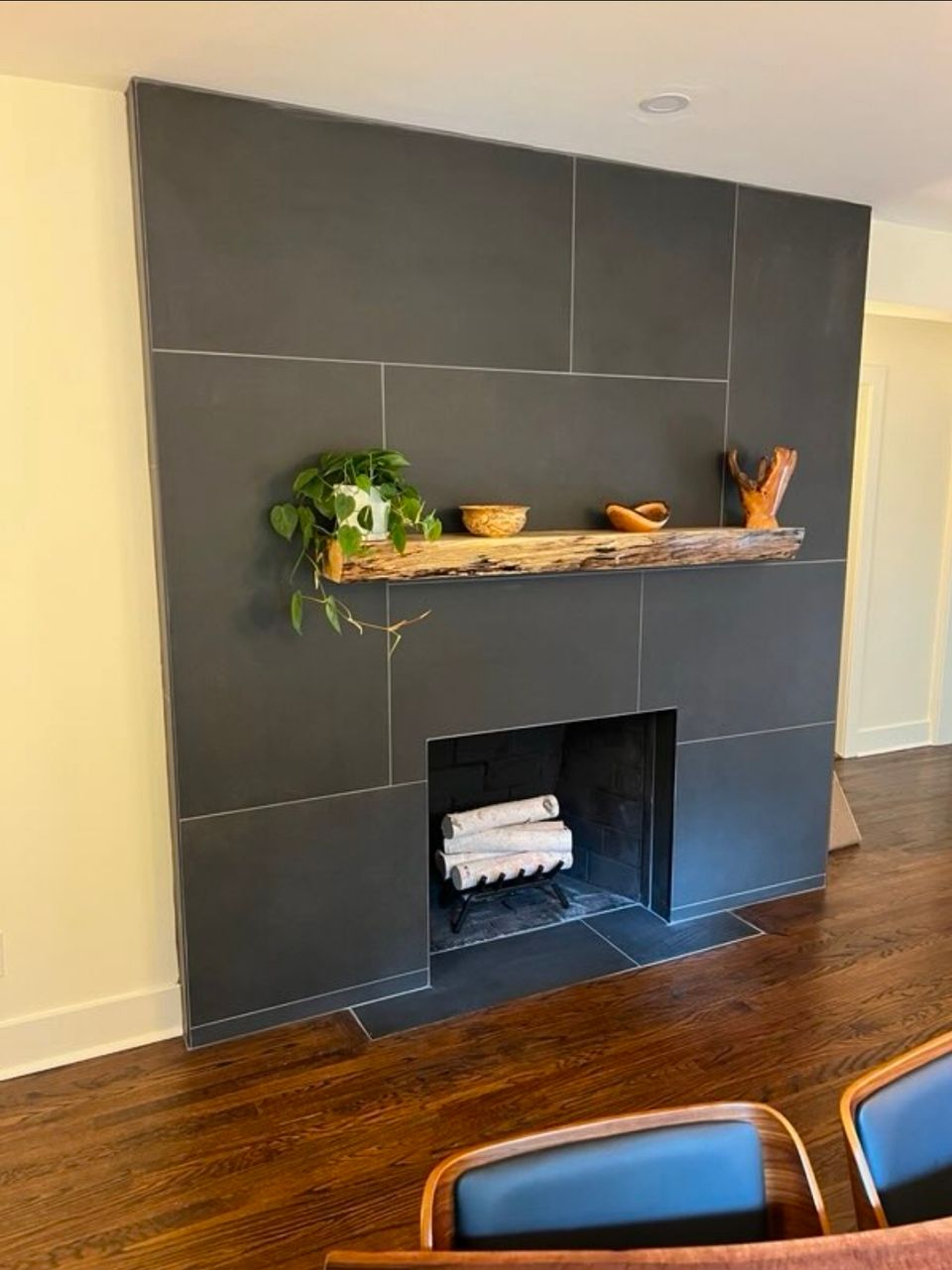 Large format charcoal tile fireplace surround with live edge wood mantel from a living room remodel