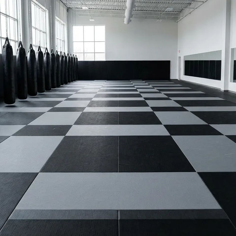 Clean and spacious martial arts training facility featuring professional floor mats, heavy punching bags, and wall mirrors for local self-defense classes.