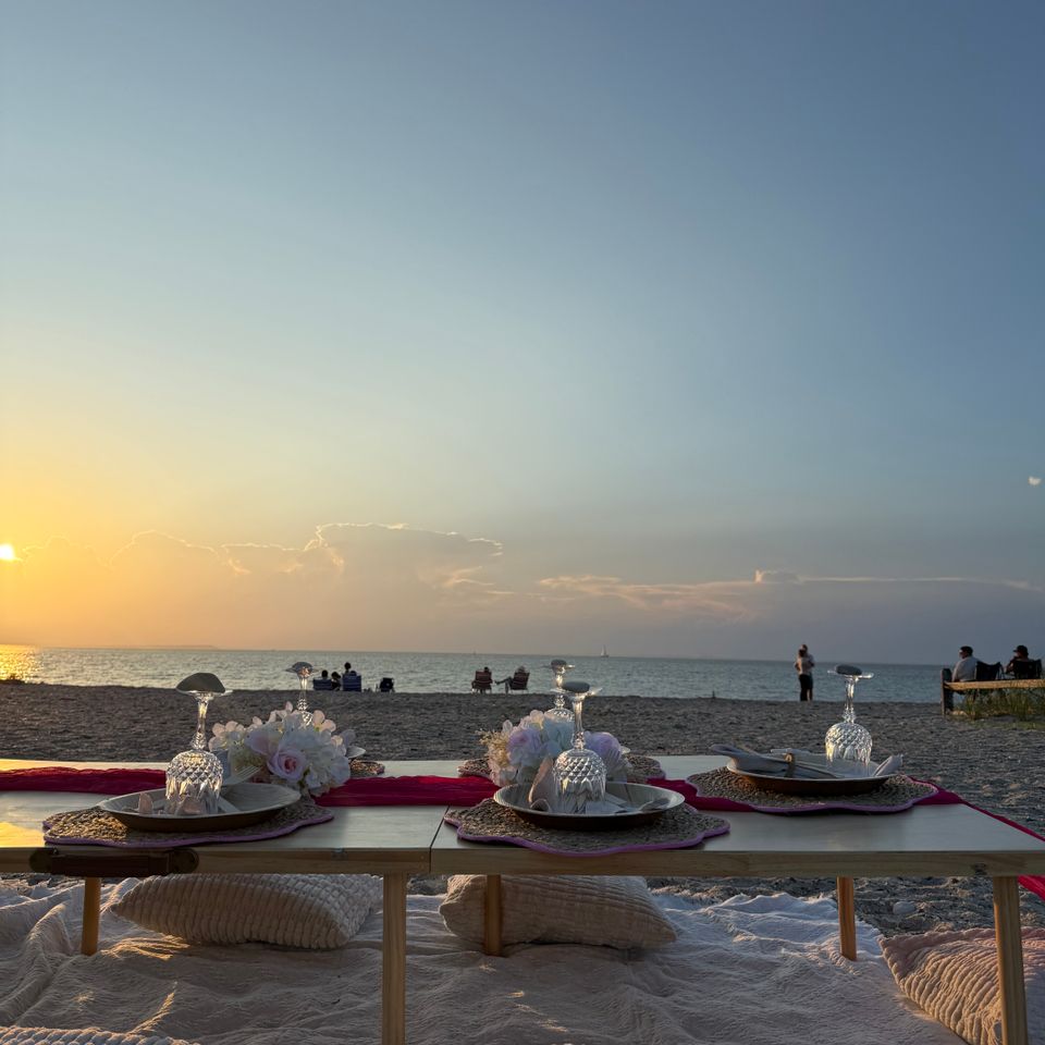 Sunset beach picnic styled with florals, glassware, and floor cushions along the Hamptons NY shore