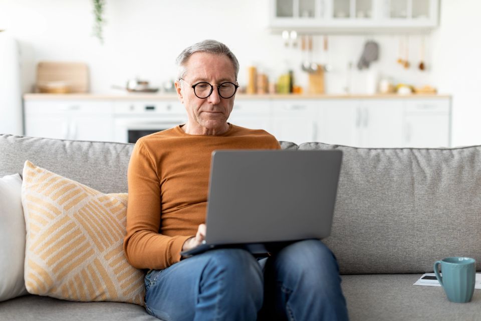 Senior man using laptop on couch with help from senior tech support on Long Island NY