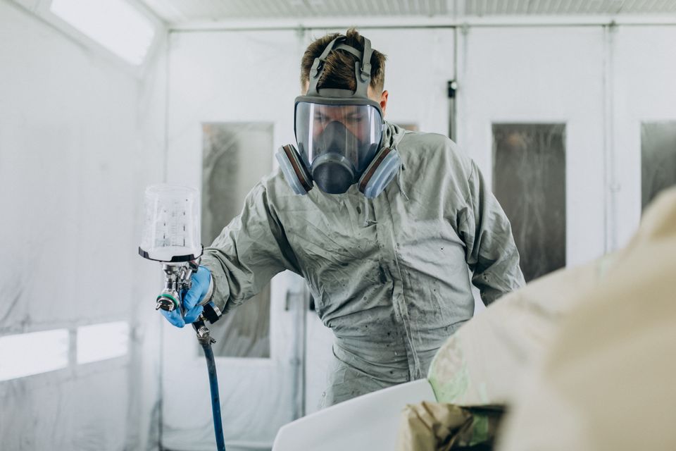 Car mechanic painting car with spray gun (1)