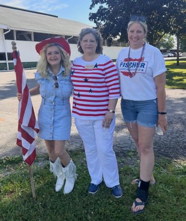 Alt Tag: Three women dressed in patriotic attire posing with an American flag at a Fourth of July event.