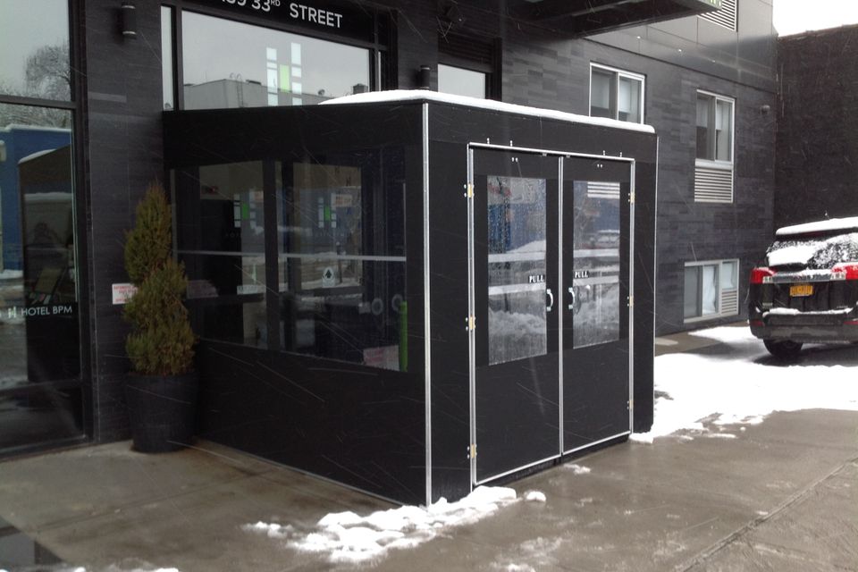 Black framed seasonal vestibule with double glass doors at a New York City building entrance, snow on the sidewalk