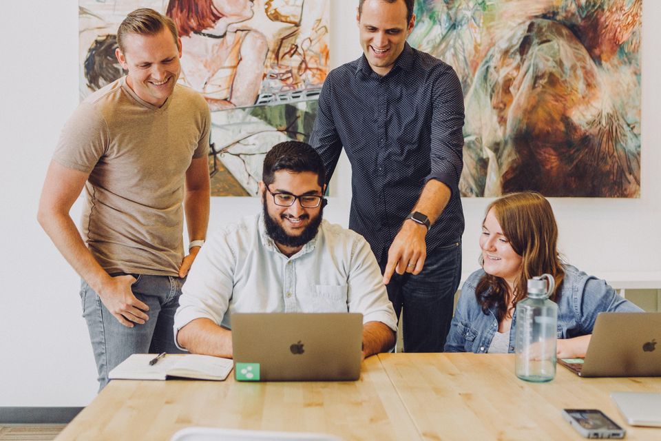 three men and one woman looking at computer