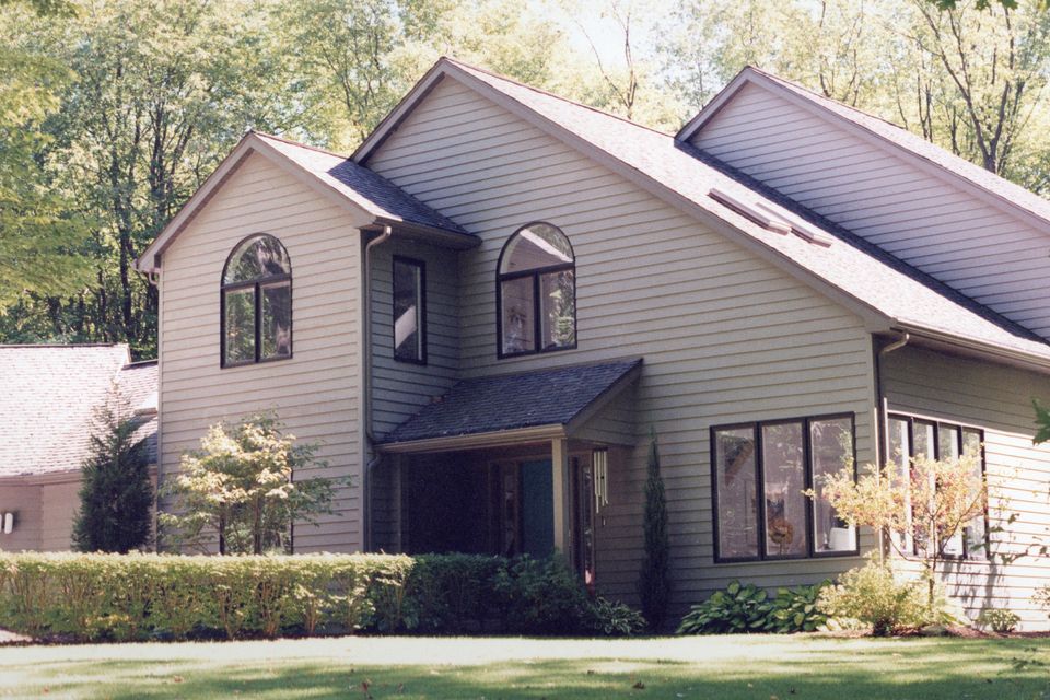 Two-story custom home featuring gray siding, large arched windows, landscaped yard, and mature trees.