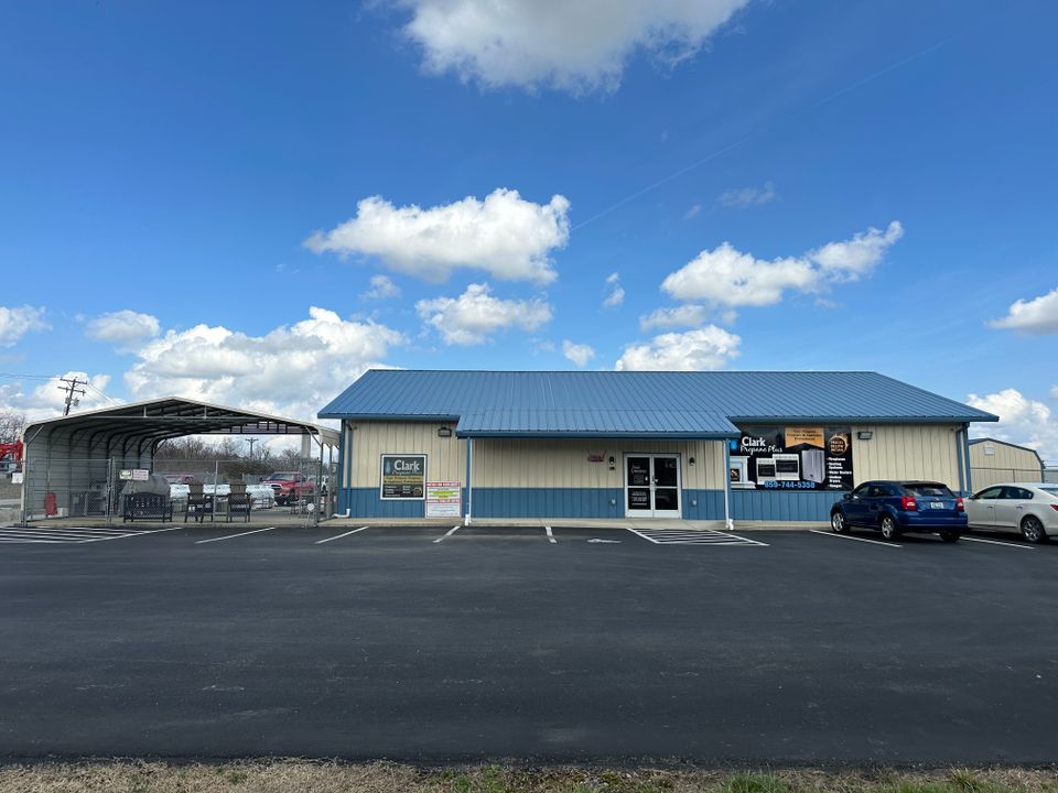 Clark Propane Plus office building with a blue roof, adjacent propane refill station near me, and parking lot under a clear, blue sky with scattered clouds.