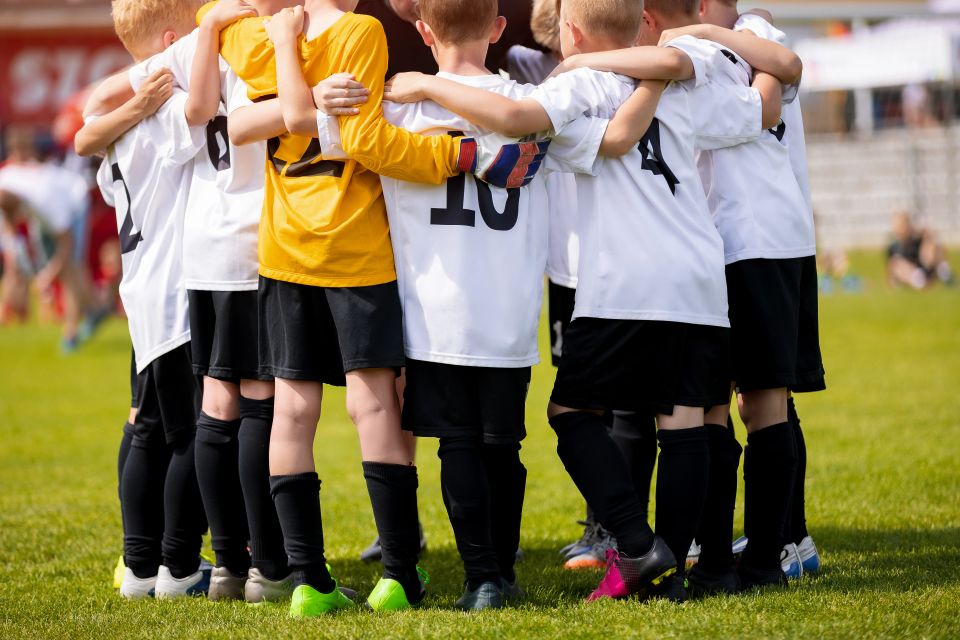 A stock image of a youth soccer team huddling with their coach on a bright, sunny field, used in a blog by Cannone Marketing.