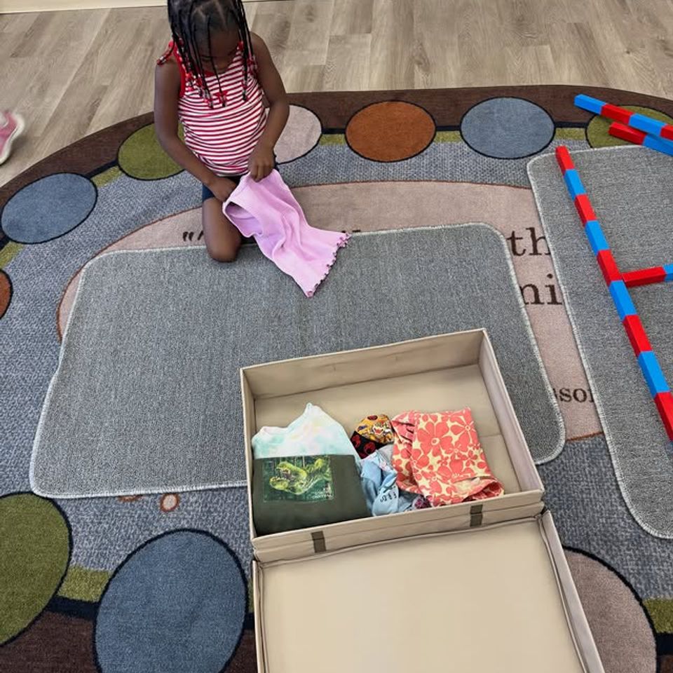 Preschool girl folding cloth napkins on the classroom rug during Montessori practical life work in Palmdale CA