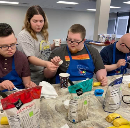 Participants with Down syndrome measuring ingredients and preparing fruit smoothies during a DSAV Cooks class.