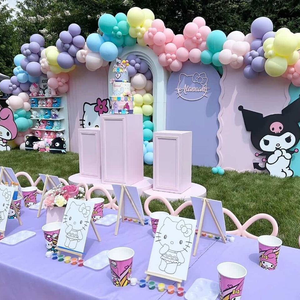 Colorful Hello Kitty and Kuromi themed birthday setup with pastel balloon garland, character backdrops, painting station, and decorated kids’ table.