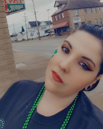 Young woman wearing green beads and shamrock face paint posing for a St. Patrick’s Day selfie.