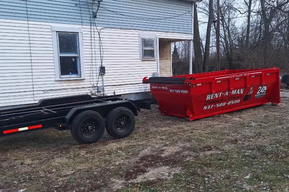 Red Rent-A-Man Dumpster Rentals dumpster beside a residential property.