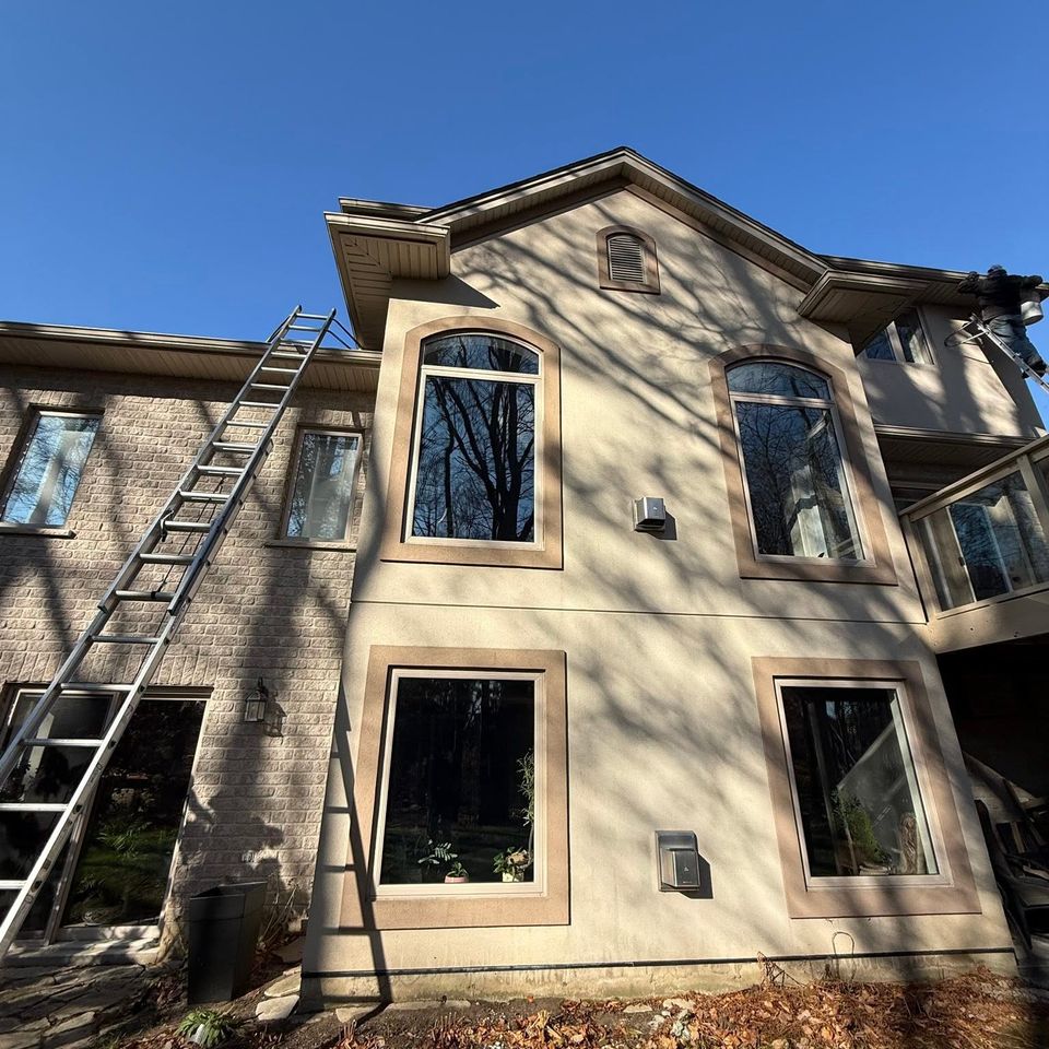 Technician on ladder cleaning gutters on two-storey stucco and brick home in Tillsonburg Ontario