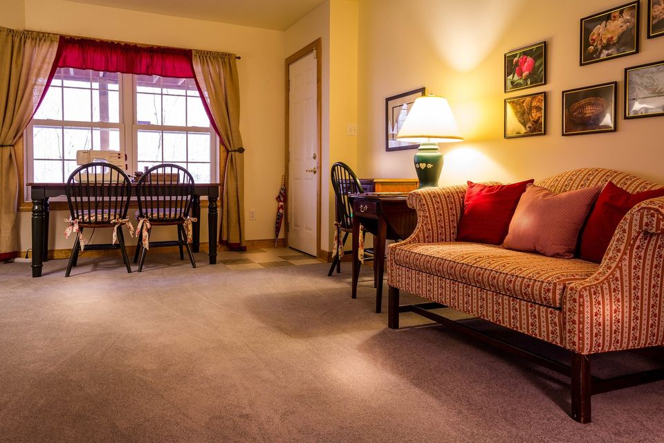 Carpet installed throughout a living room with a patterned sofa, dining table, and chairs.